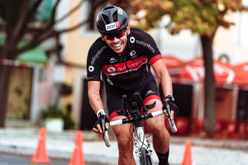 Smiling cyclist in helmet racing on road bike during a sunny day.