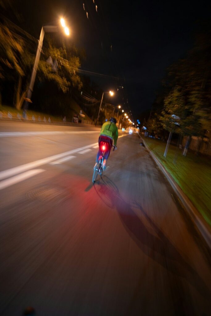 A nighttime urban scene with a bike, sculpture, and a passing truck on a road.
