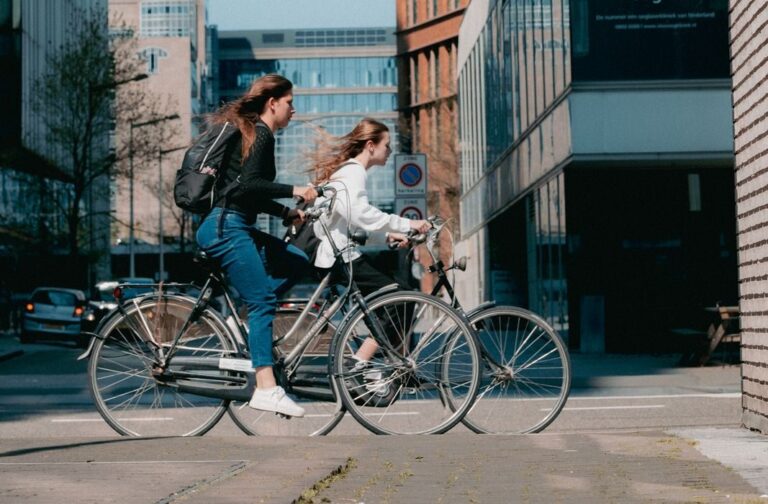 To unge kvinder cykler i byen ved dagslys