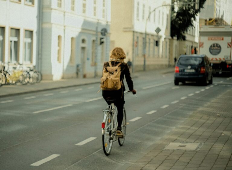 Kvinde med rygsæk cykler i byen ved dagslys